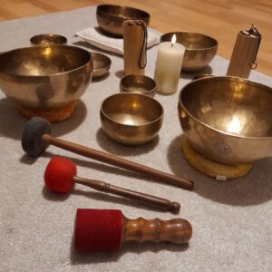 Klangschalen-Set für Klangmassage und Entspannungstherapie mit Schlägeln, Koshi-Klangspiel und brennender Kerze auf einer Matte bei Farbe und Klang Leipzig.